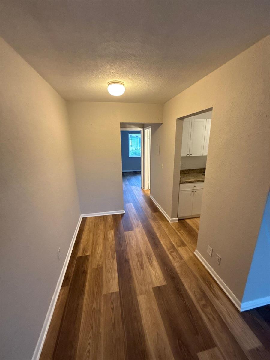 A hallway with wood-look flooring leads to a doorway and a small kitchen area — 717 NE 10th Avenue # 06, Boynton Beach FL 33435, BOYNTON BEACH, FL