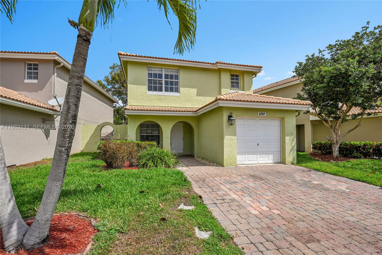 A two-story light green house features a paved driveway, a garage, and a palm tree — 6767 Duval Ave, West Palm Beach FL 33411, WEST PALM BEACH, FL