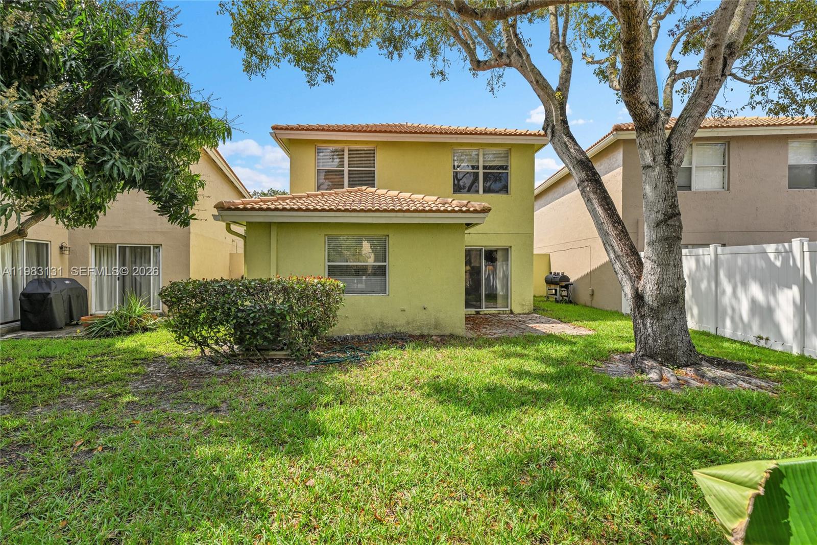 The exterior of a two-story yellow house features a tiled roof and a grassy backyard — 6767 Duval Ave, West Palm Beach FL 33411, WEST PALM BEACH, FL