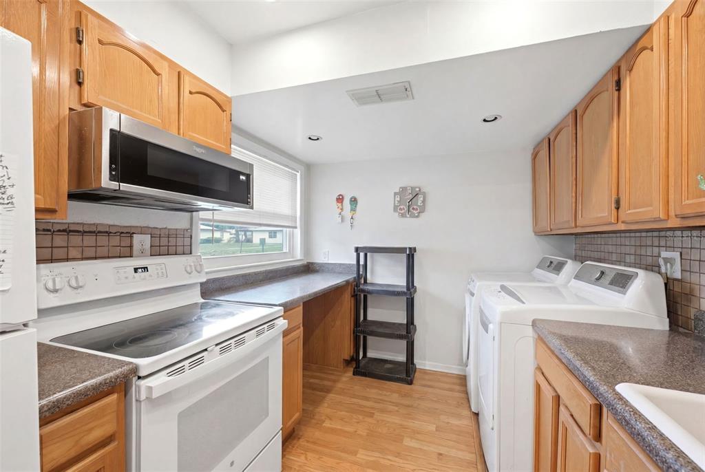 A kitchen and laundry area features wood cabinets, a white stove, and white appliances — 24862 US HIGHWAY 19 N UNIT 3506, CLEARWATER, FL