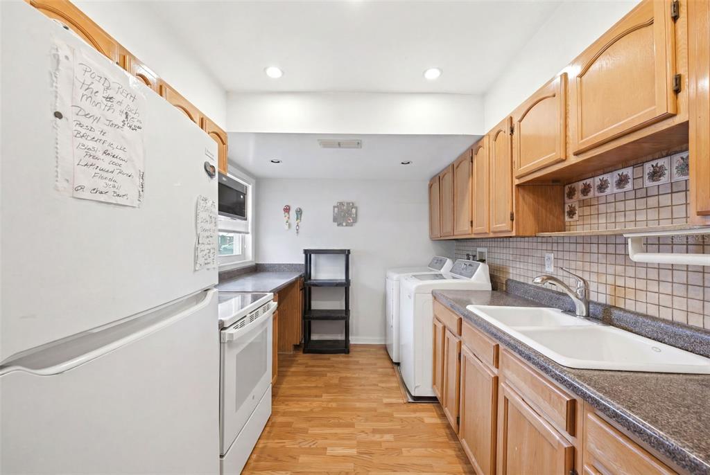 A kitchen with wooden cabinets, white appliances, a double sink, and laundry machines — 24862 US HIGHWAY 19 N UNIT 3506, CLEARWATER, FL