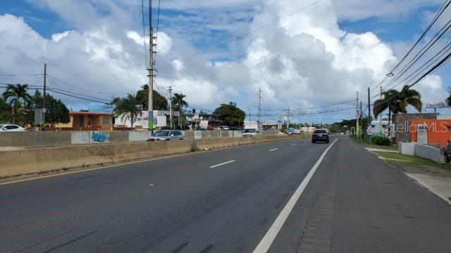 A view of a multi-lane road with utility poles, palm trees, and buildings under a cloudy sky — State Road PR-2 KM. 94.0, CAMUY, PR
