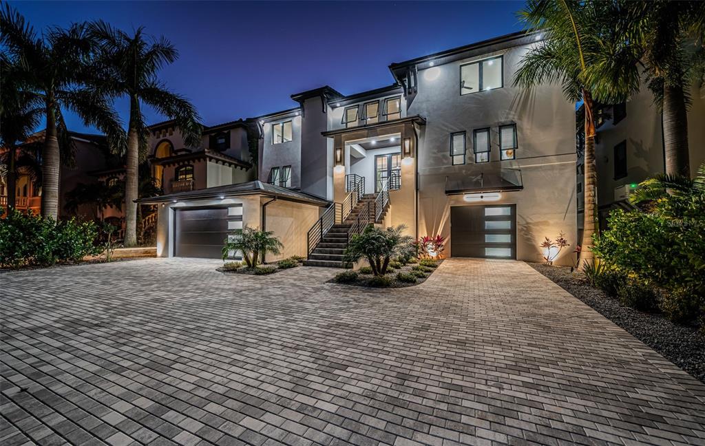 A modern multi-story house exterior at night with a paved driveway and two garages — 218 SYDNEY LANE, REDINGTON SHORES, FL