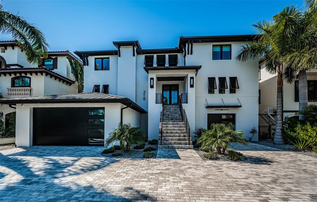 A modern white multi-story house features a black garage door and a stone staircase entrance — 218 SYDNEY LANE, REDINGTON SHORES, FL