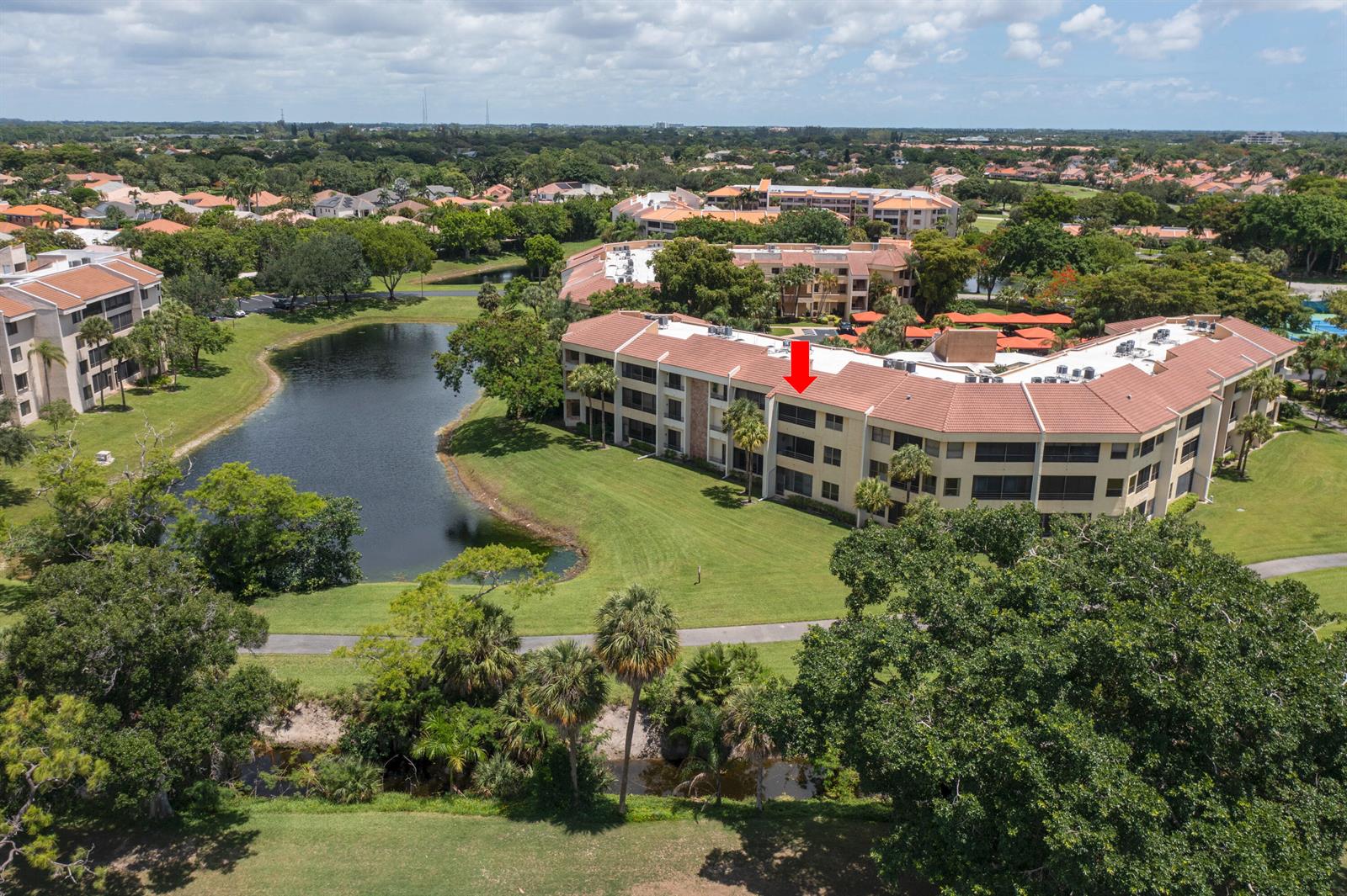 An aerial view shows a multi-story apartment building with a red tile roof near a pond — 7520 La Paz Boulevard # 104, Boca Raton FL 33433, BOCA RATON, FL