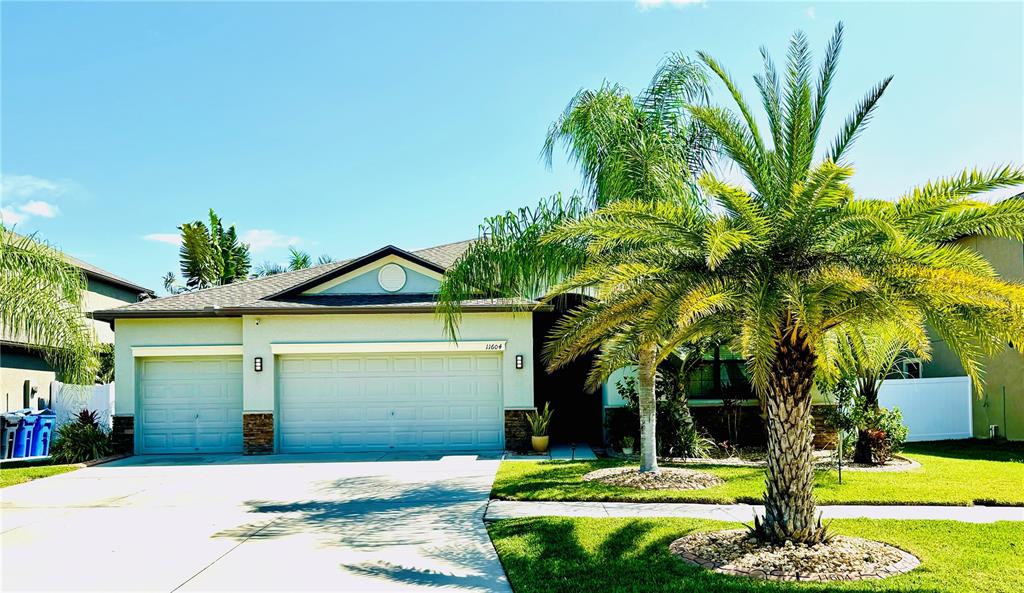 A single-story house with a three-car garage and a large palm tree in the front — 11604 SUNBURST MARBLE ROAD, RIVERVIEW, FL