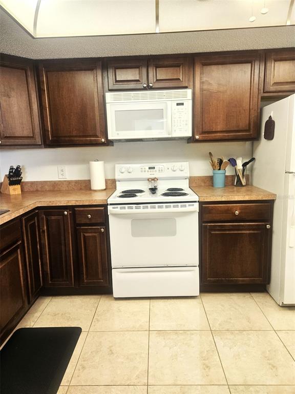 A kitchen features dark wood cabinets, white appliances, and light-colored tile flooring — 307 PINE HOLLOW CIRCLE UNIT 307, ENGLEWOOD, FL