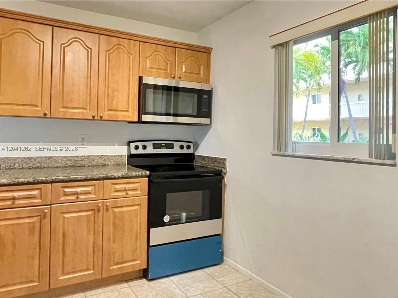 A kitchen features wood cabinets, a black stove, a stainless steel microwave, and a window — 7730 Camino Real # F113, Miami FL 33143, MIAMI, FL