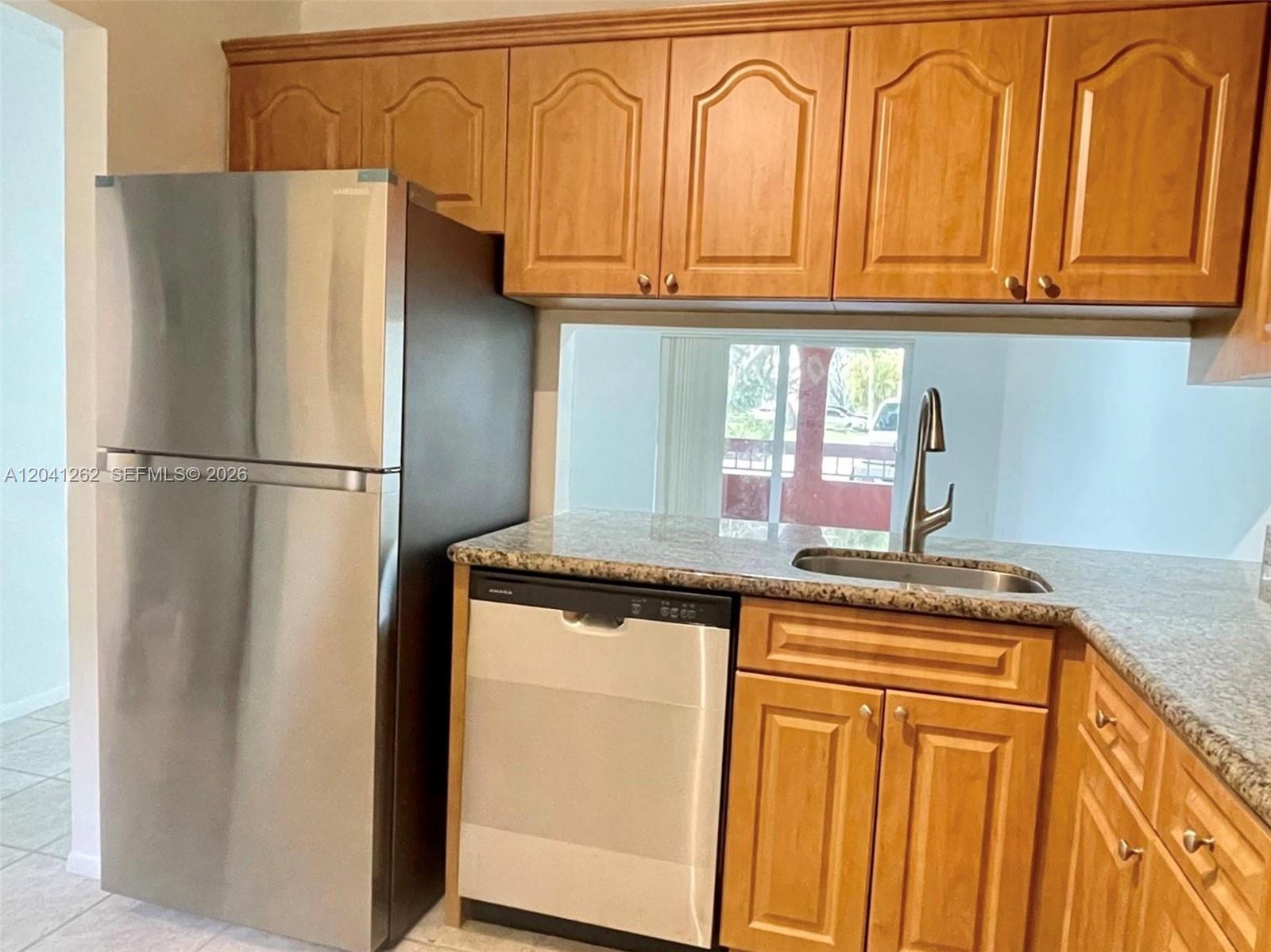 A kitchen features wood cabinets, a stainless steel refrigerator, a dishwasher, and a granite countertop — 7730 Camino Real # F113, Miami FL 33143, MIAMI, FL