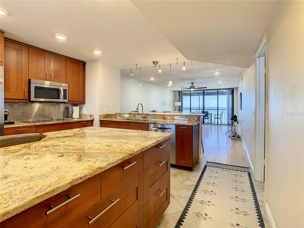 A kitchen with wood cabinets and granite countertops overlooks a living area with balcony access — 18304 GULF BOULEVARD UNIT 516, REDINGTON SHORES, FL