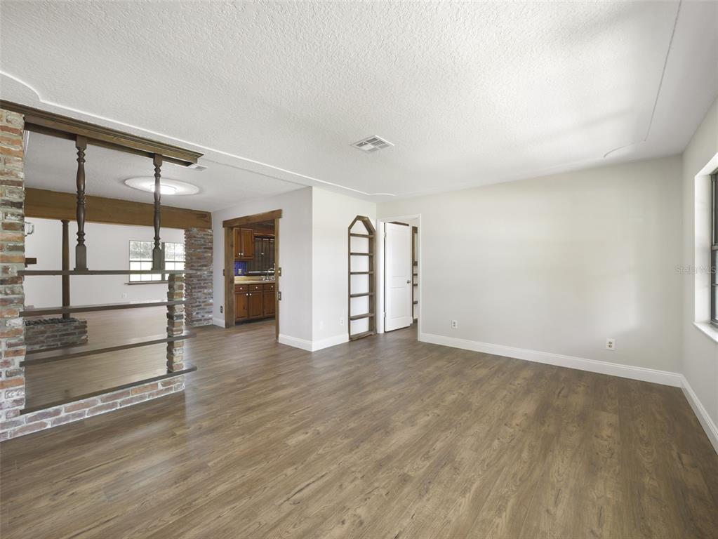 An interior view of a living area featuring wood-look flooring and a brick fireplace partition — 7107 LEIGHTON WAY, ORLANDO, FL