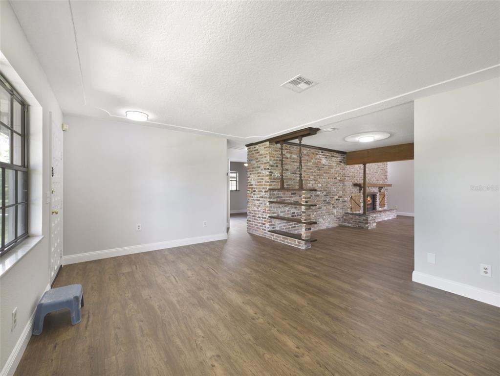 A living room features wood-look flooring, a brick room divider, and an arched shelving unit — 7107 LEIGHTON WAY, ORLANDO, FL