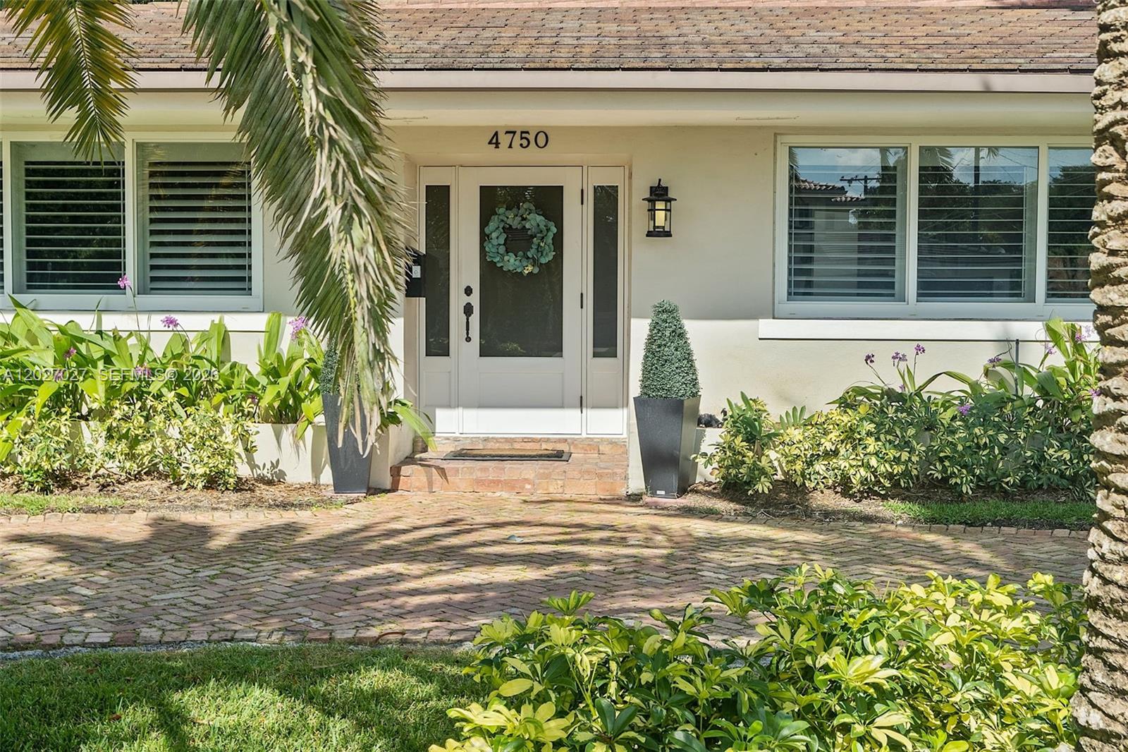 The exterior of a house features a brick driveway, a white front door, and landscaping — 4750 Alhambra Cir, Coral Gables FL 33146, CORAL GABLES, FL