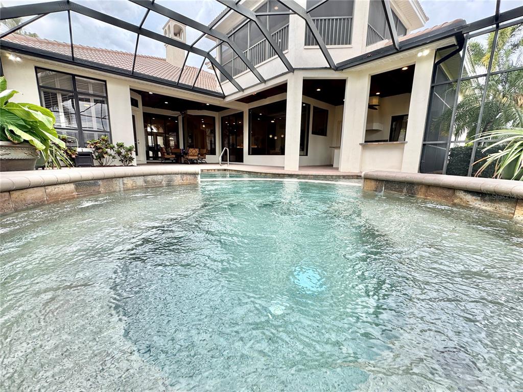A swimming pool with a spillover spa is enclosed by a screened lanai — 6919 DOMINION LANE, LAKEWOOD RANCH, FL