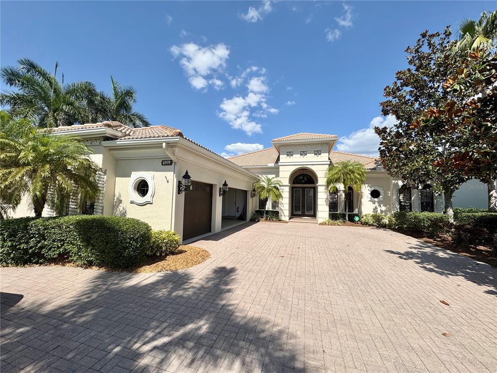 A single-story house with a paved driveway, a three-car garage, and a tiled roof — 6919 DOMINION LANE, LAKEWOOD RANCH, FL