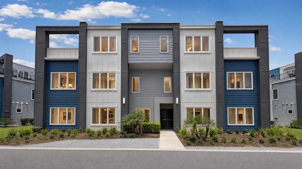 A three-story apartment building features blue and gray siding with large windows and balconies — 7740 SANDY RIDGE DRIVE UNIT 135, REUNION, FL