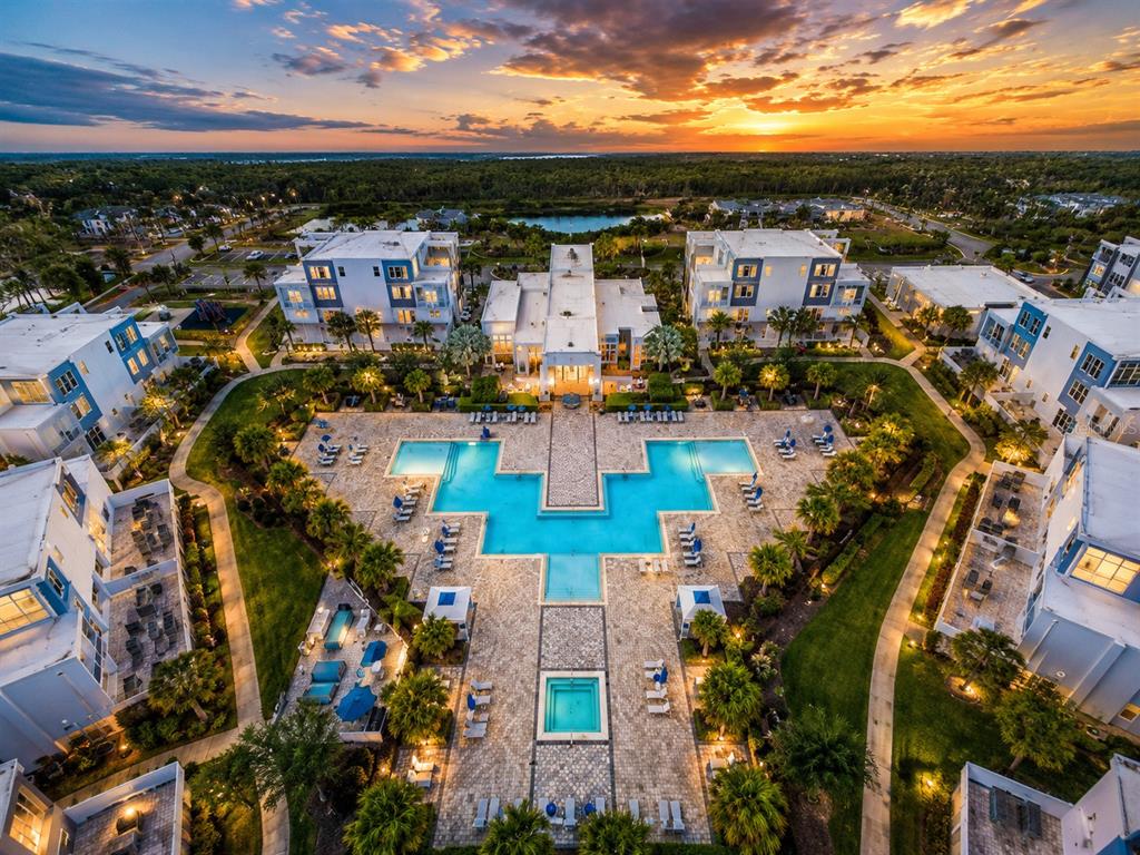 An aerial view of a resort-style apartment complex featuring a large pool and sunset sky — 7740 SANDY RIDGE DRIVE UNIT 135, REUNION, FL