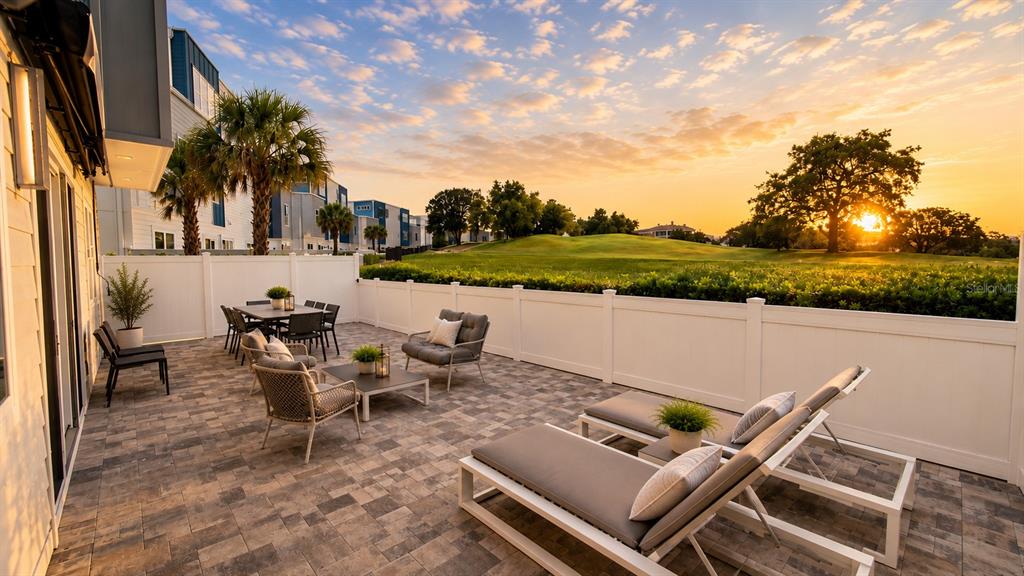 A paved patio features outdoor furniture, a white privacy fence, and a view of a golf course — 7740 SANDY RIDGE DRIVE UNIT 135, REUNION, FL