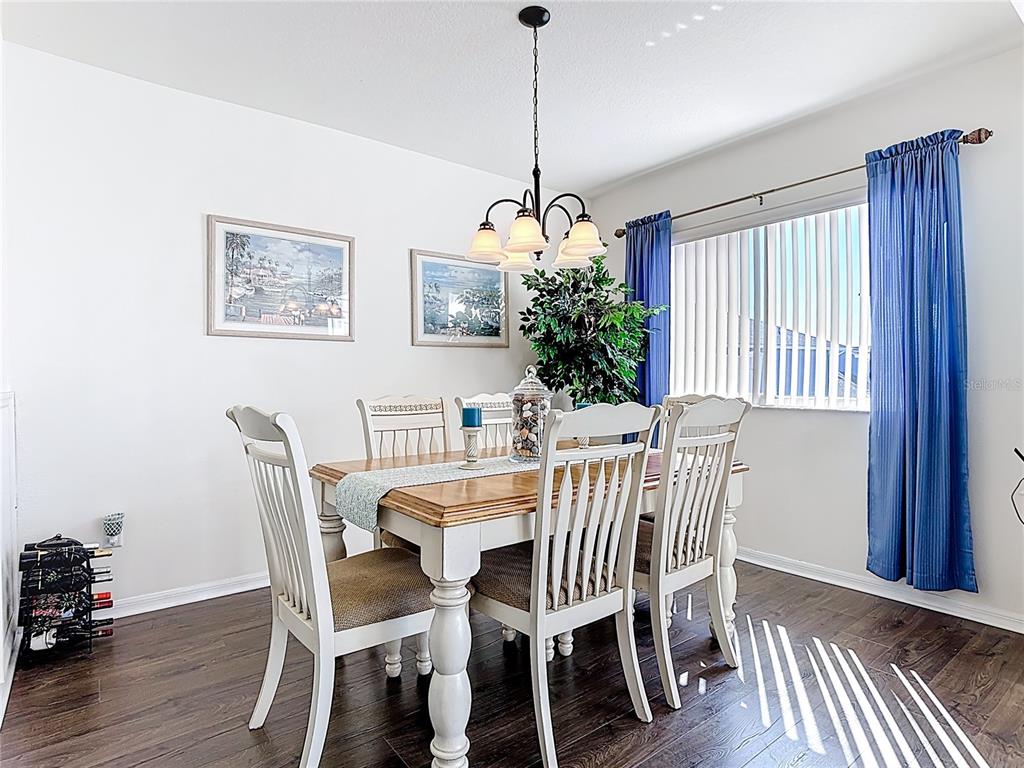 A dining room features a wooden table with white chairs, a chandelier, and blue curtains — 565 ORCHID DRIVE, DAVENPORT, FL