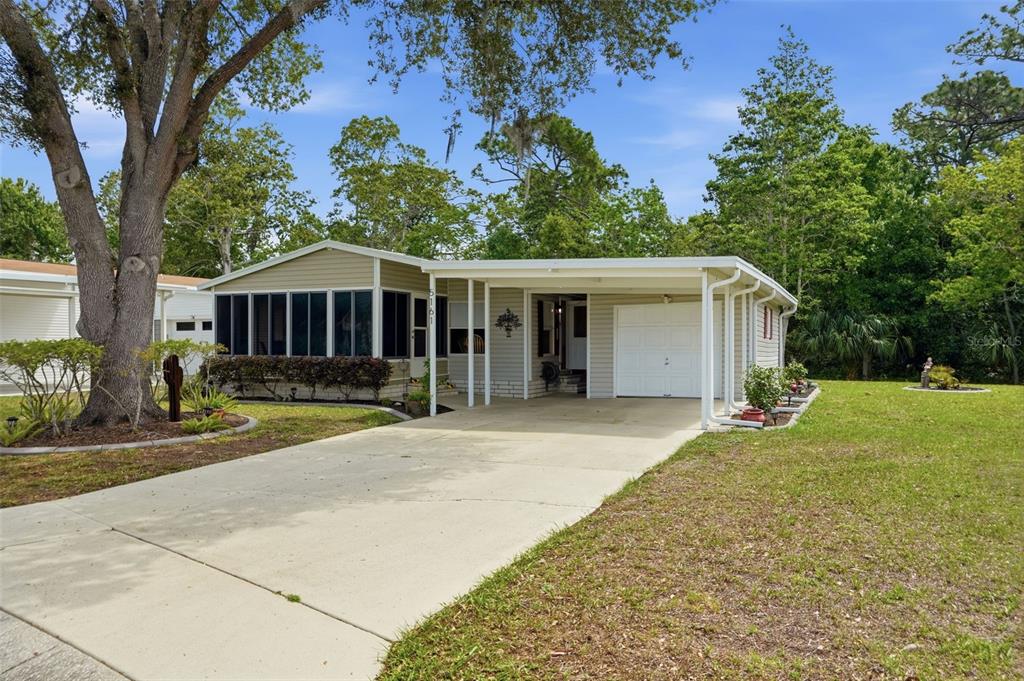 A single-story house with a screened porch, carport, and concrete driveway under a large tree — 5161 FOREST GLENN DRIVE, SPRING HILL, FL