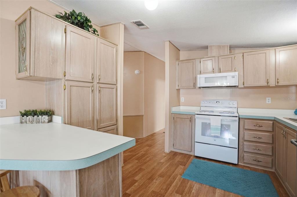 A kitchen features light wood cabinets, white countertops, white appliances, and wood-look flooring — 5161 FOREST GLENN DRIVE, SPRING HILL, FL
