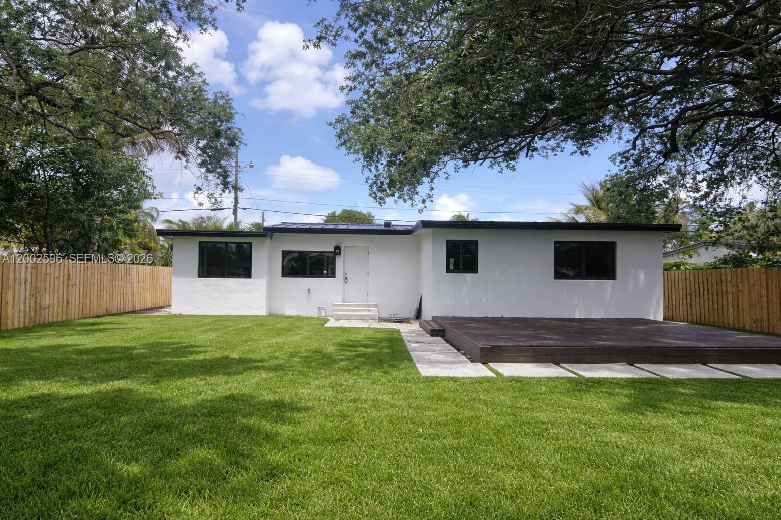 A white house with a dark roof and deck sits in a grassy fenced yard — 1242 NE 145th St, Miami FL 33161, MIAMI, FL