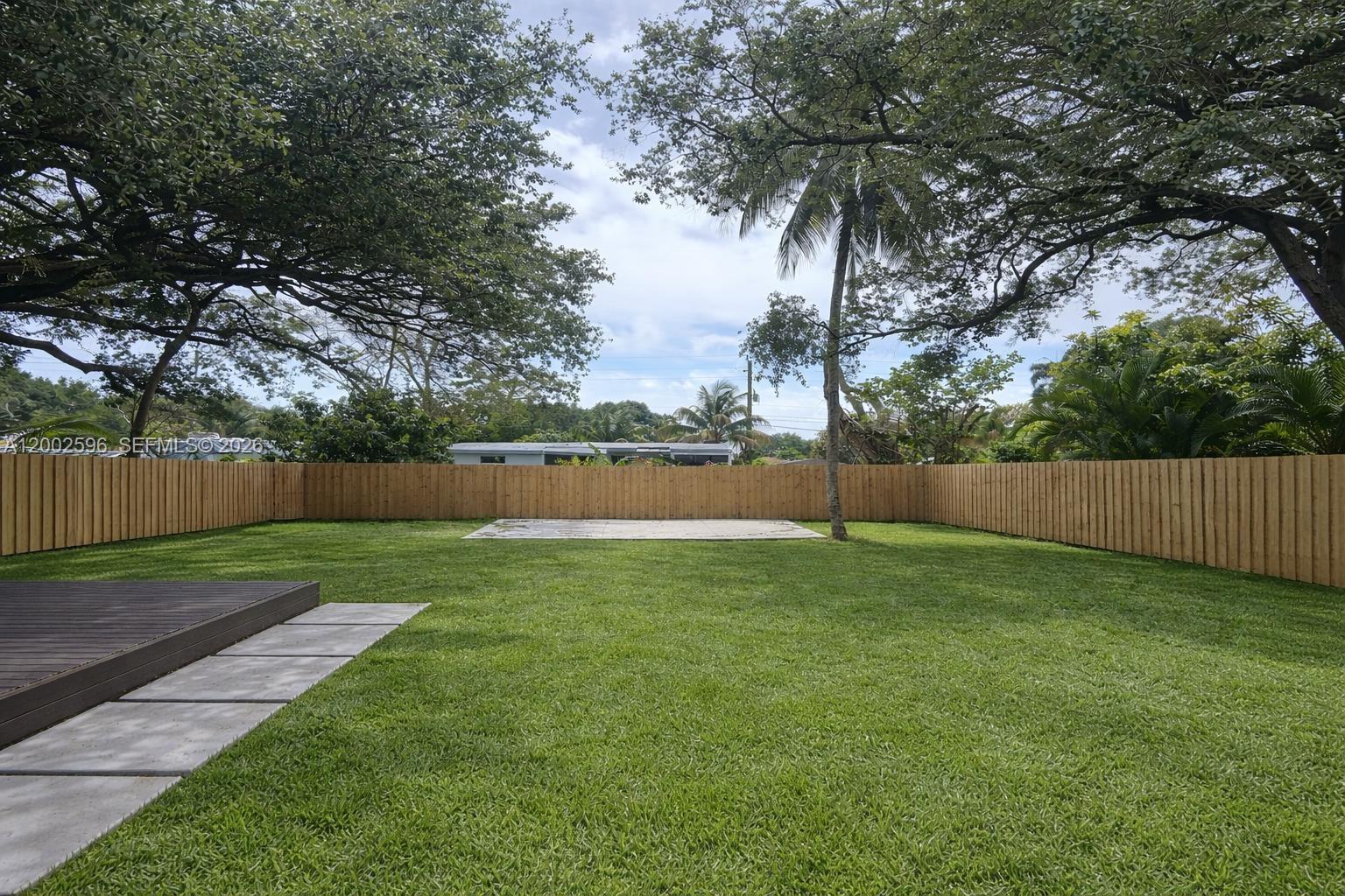 A fenced backyard features a green lawn, a wooden deck, and a concrete patio area — 1242 NE 145th St, Miami FL 33161, MIAMI, FL