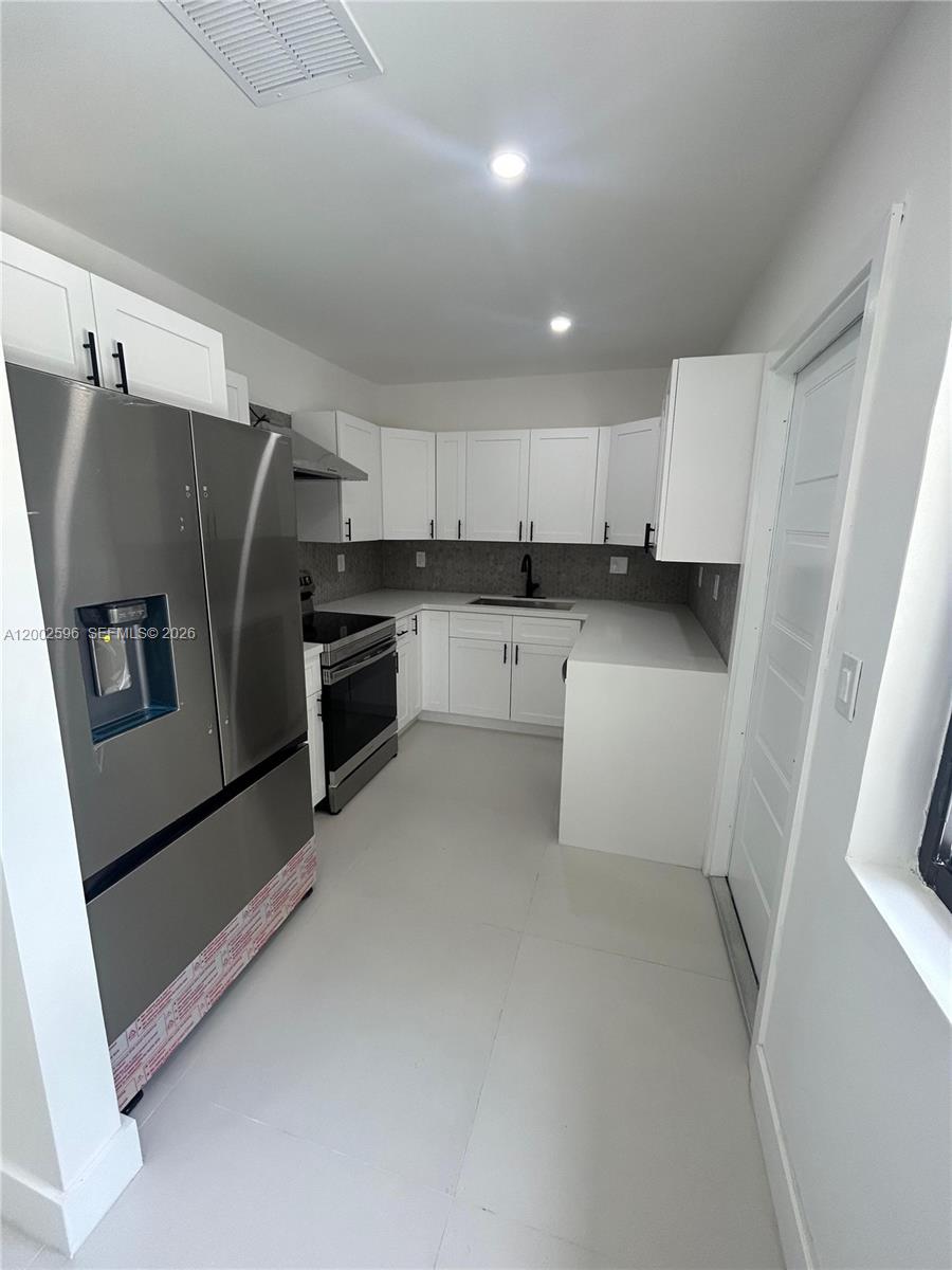 A modern kitchen features white cabinets, stainless steel appliances, and light-colored tile flooring — 1242 NE 145th St, Miami FL 33161, MIAMI, FL