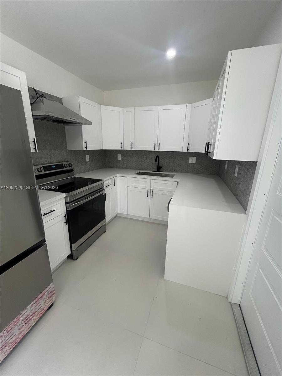 A kitchen features white cabinets, stainless steel appliances, and a gray tiled backsplash — 1242 NE 145th St, Miami FL 33161, MIAMI, FL