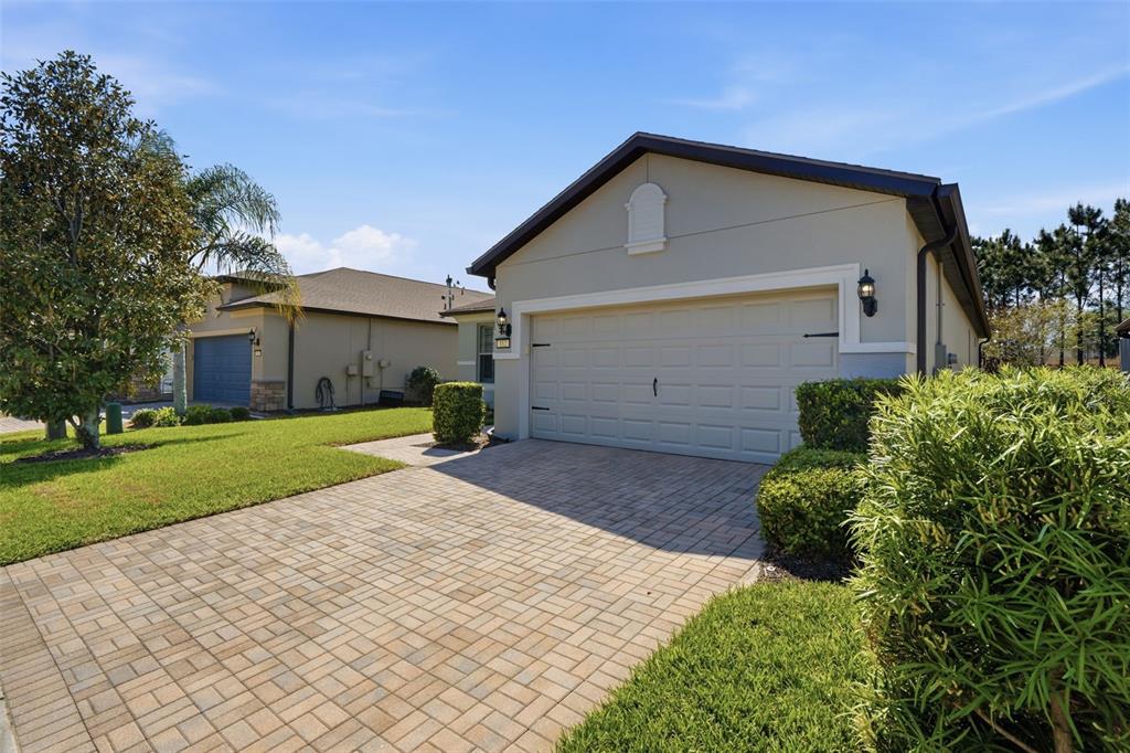 A beige house with a paver driveway and a two-car garage under a blue sky — 112 CASTELLON COURT, DAVENPORT, FL