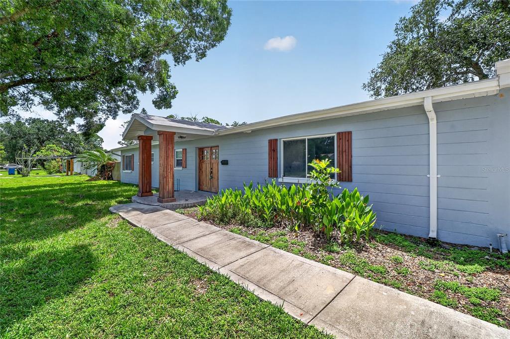 A light blue house exterior features a concrete walkway leading to a covered wooden porch — 120 81ST AVENUE NE, ST PETERSBURG, FL