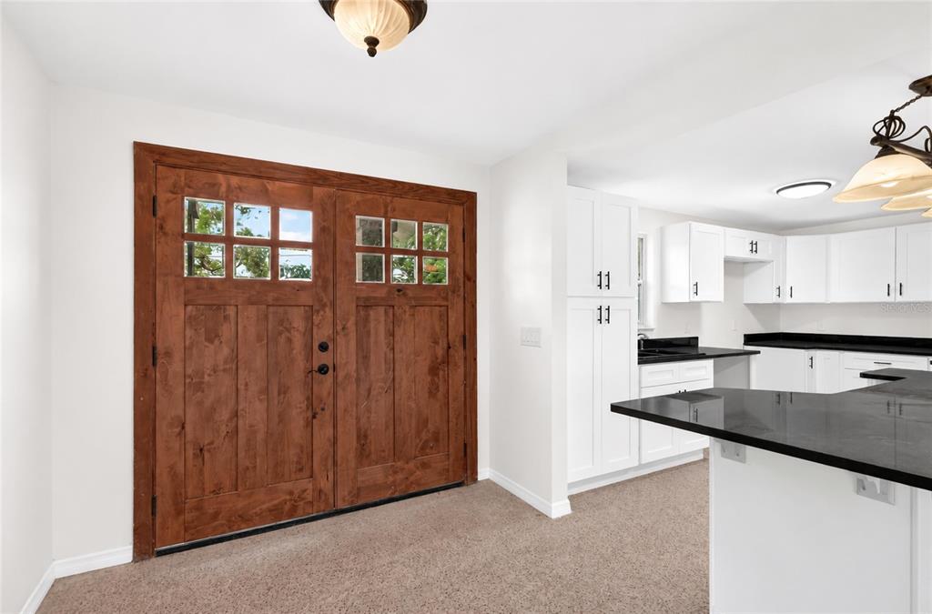 A room with carpeted flooring features a wooden double door and an adjacent white kitchen — 120 81ST AVENUE NE, ST PETERSBURG, FL