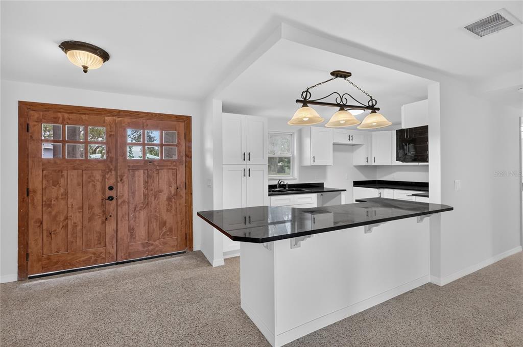 A kitchen with white cabinets, black countertops, and a breakfast bar next to a wooden door — 120 81ST AVENUE NE, ST PETERSBURG, FL