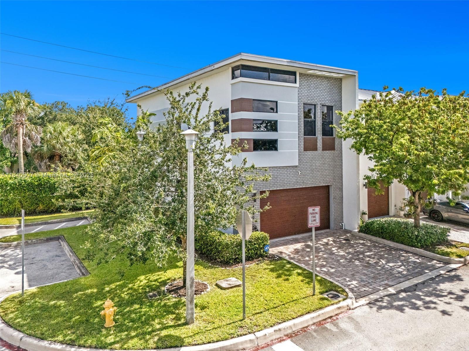 A two-story modern townhouse with a brick facade, wood-toned garage door, and a paved driveway — 4460 NW 8th Pl, Plantation FL 33317, PLANTATION, FL