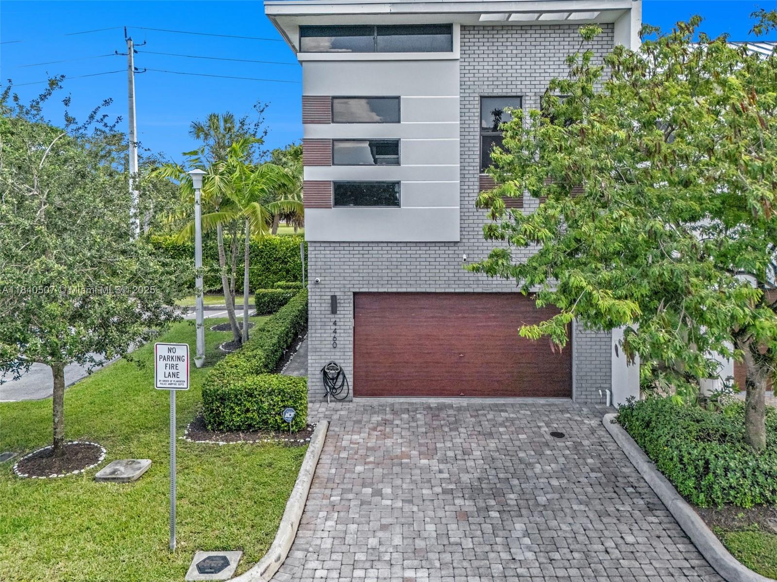 A modern two-story house with a brick facade, wood-toned garage door, and a paved driveway — 4460 NW 8th Pl, Plantation FL 33317, PLANTATION, FL
