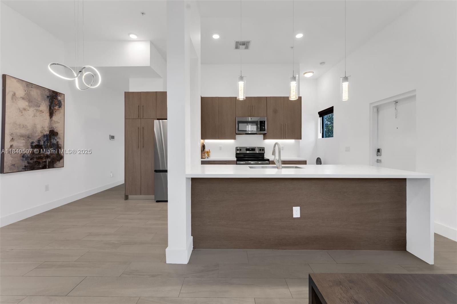 A modern kitchen features wood-toned cabinetry, white countertops, a central island, and light-colored flooring — 4460 NW 8th Pl, Plantation FL 33317, PLANTATION, FL