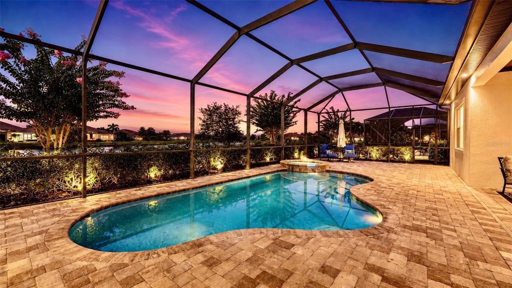 A screened-in pool and spa area with paver decking at sunset — 7005 WHITTLEBURY TRAIL, LAKEWOOD RANCH, FL