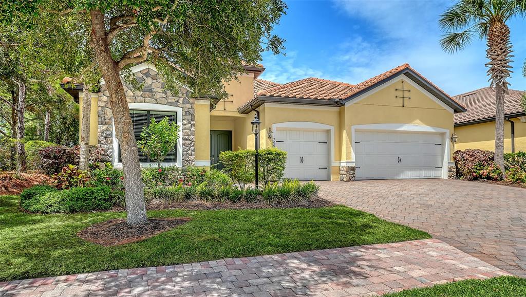 A single-story house with a stone facade, yellow stucco walls, and a three-car garage — 7005 WHITTLEBURY TRAIL, LAKEWOOD RANCH, FL