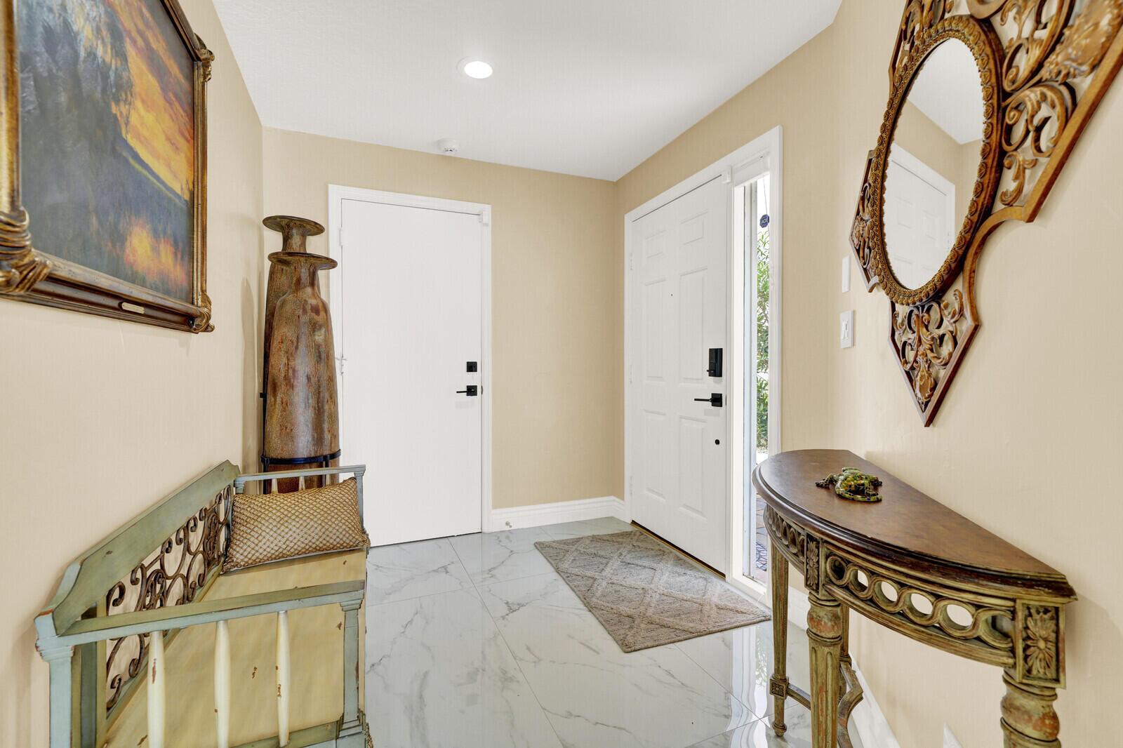 An entryway features a white door, marble-look tile flooring, a console table, and a mirror — 8634 Vía Reale # 1, FL 33496, FL