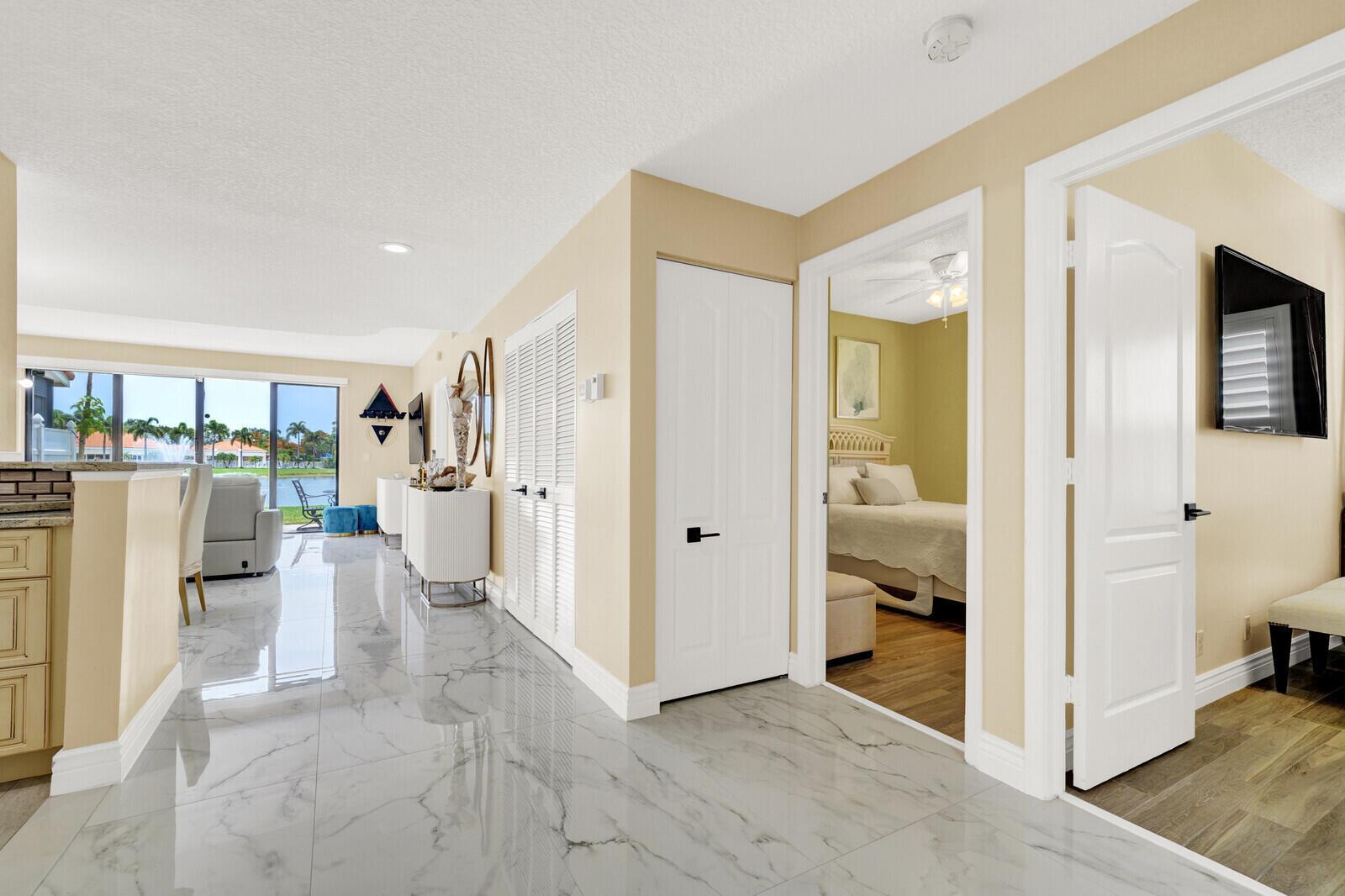 A hallway with white tile floors leads to a living area overlooking a lake view — 8634 Vía Reale # 1, FL 33496, FL