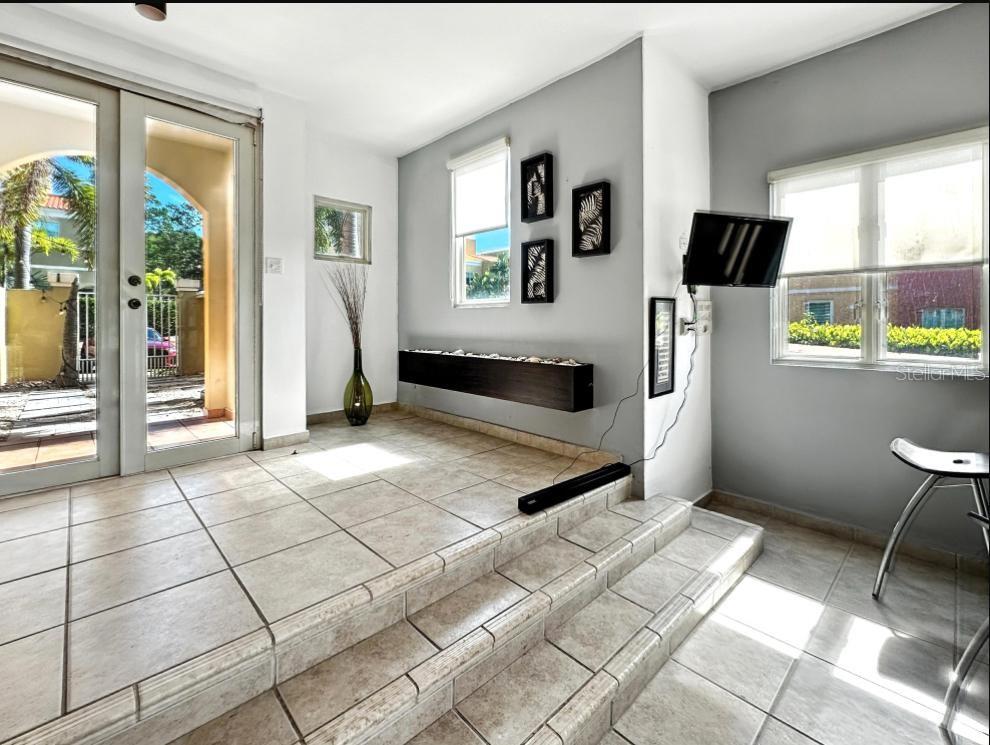 A sunroom with tiled floors, a step-down level, a wall-mounted television, and glass patio doors — VIA CAPRI # 8 AQUABELLA UNIT 117, HUMACAO, PR
