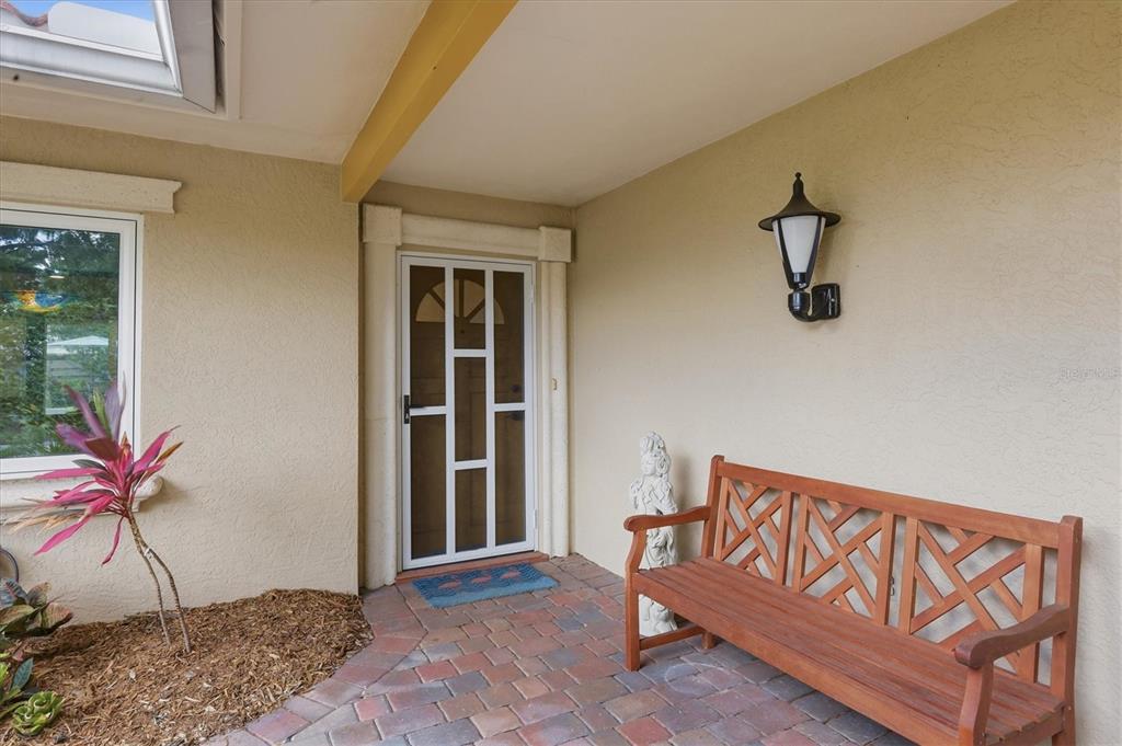 A covered entryway features a brick patio, a wooden bench, and a white storm door — 3504 BROOKLINE DRIVE, SARASOTA, FL