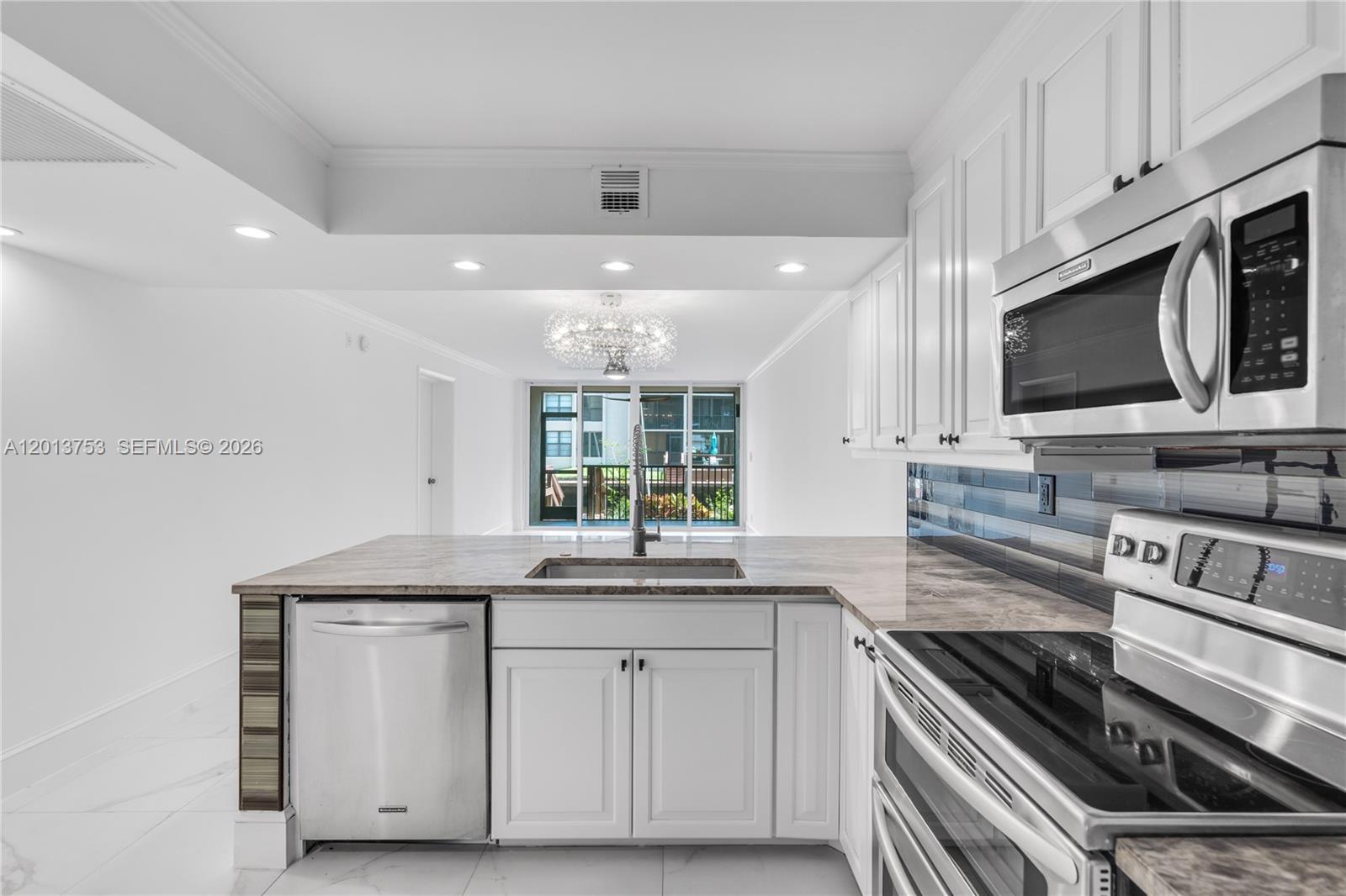 A modern kitchen features white cabinets, stainless steel appliances, and a view toward a balcony — 12 Royal Palm Way # 103, Boca Raton FL 33432, BOCA RATON, FL