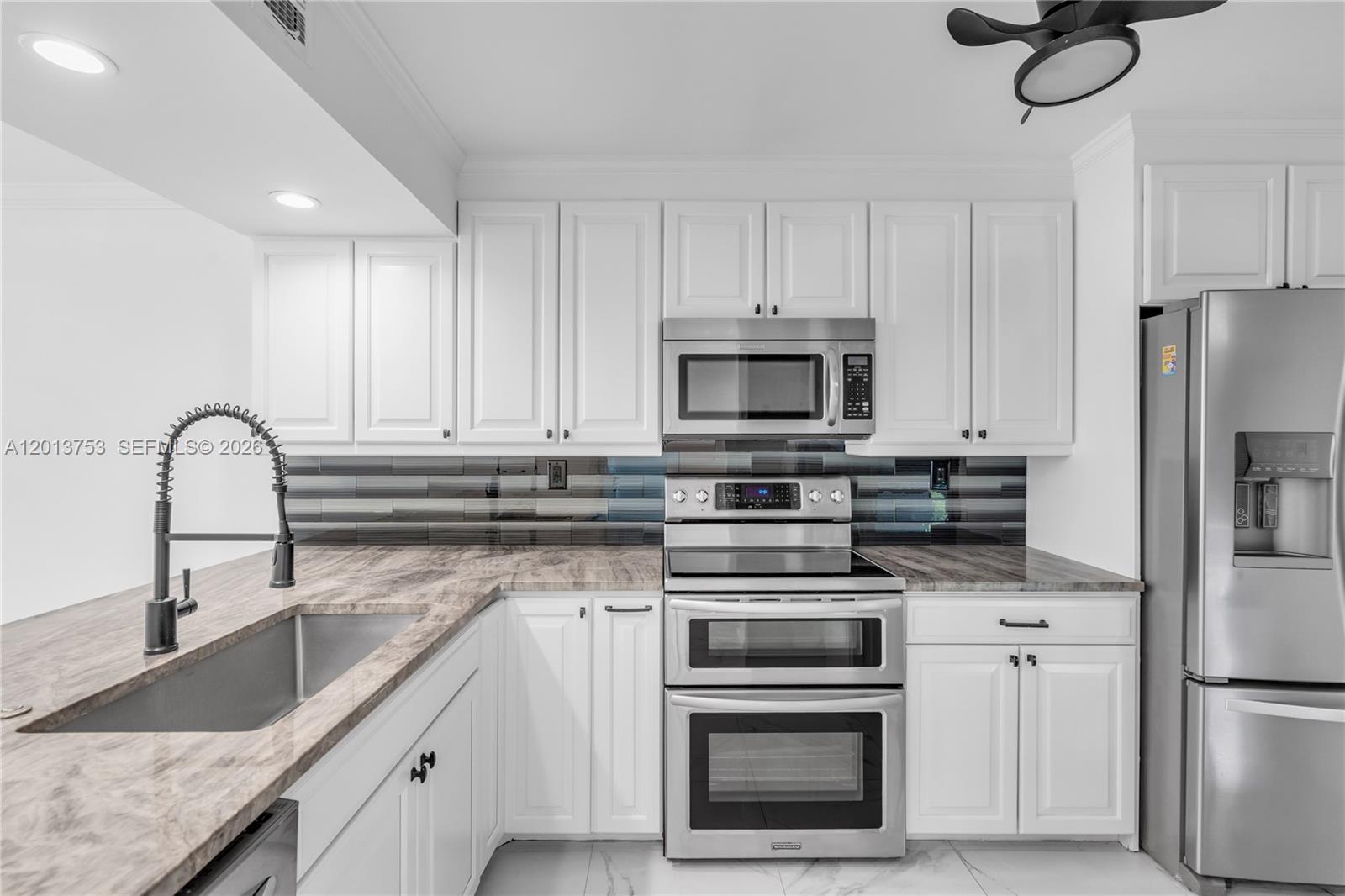 A kitchen features white cabinets, stainless steel appliances, a dark backsplash, and marble-patterned countertops — 12 Royal Palm Way # 103, Boca Raton FL 33432, BOCA RATON, FL