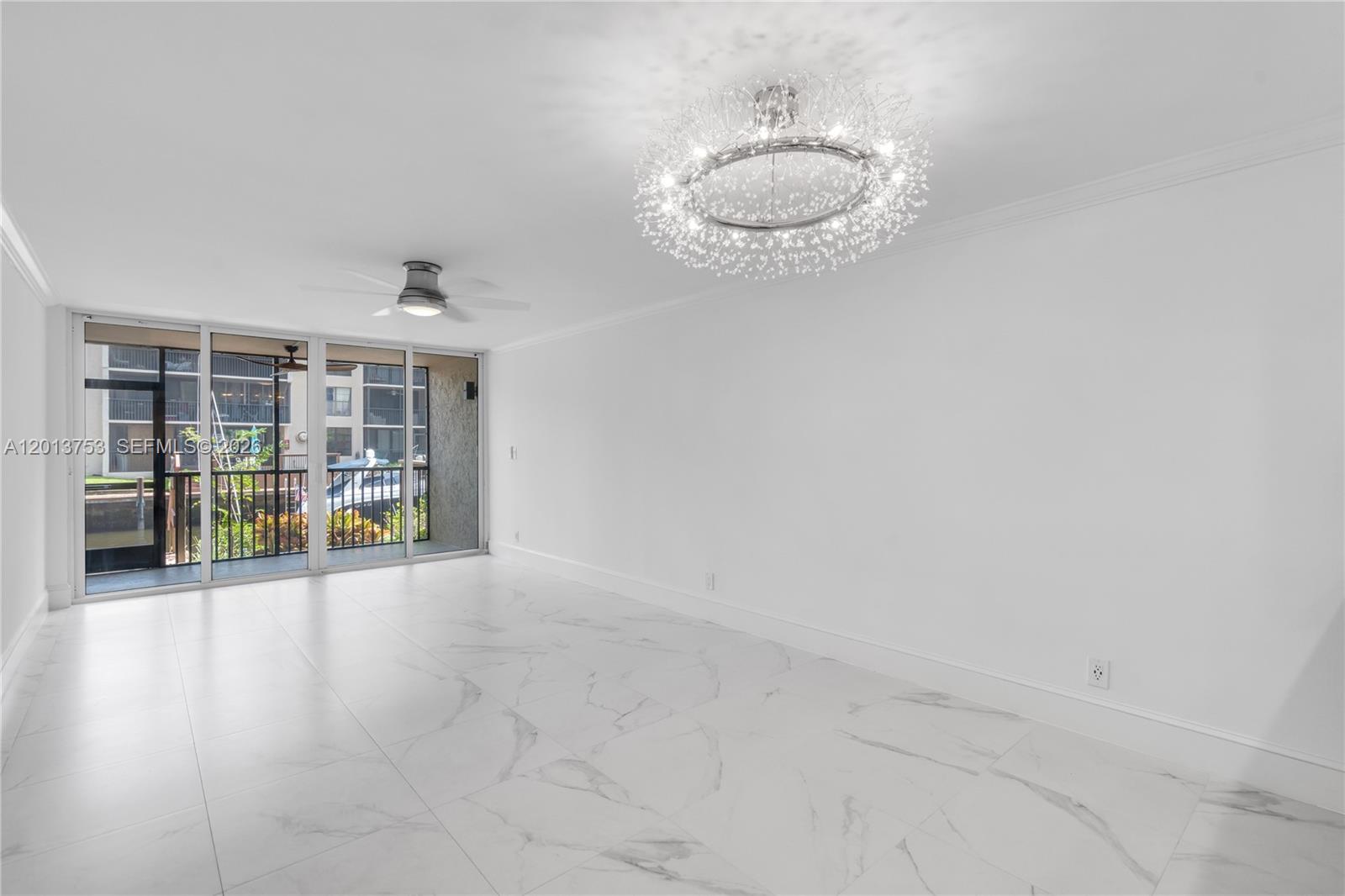 A bright, empty room features white marble-look tile flooring, a modern chandelier, and sliding glass doors — 12 Royal Palm Way # 103, Boca Raton FL 33432, BOCA RATON, FL
