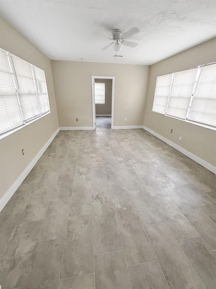 An empty room features light-colored tile flooring, beige walls, and windows with white blinds — 3045 NW 68th Street NW, Miami FL 33147, MIAMI, FL