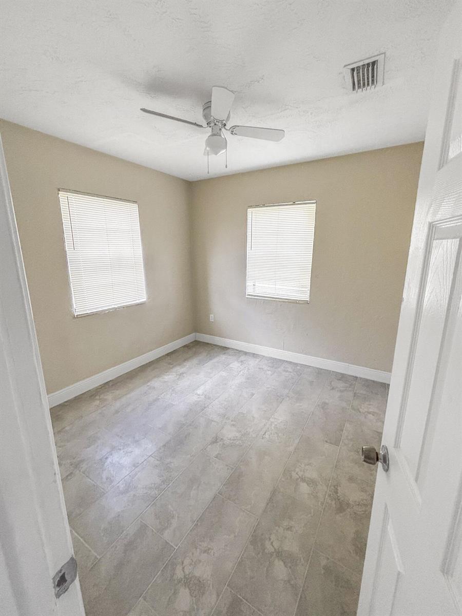 A small bedroom with beige walls, tile flooring, two windows with blinds, and a ceiling fan — 3045 NW 68th Street NW, Miami FL 33147, MIAMI, FL