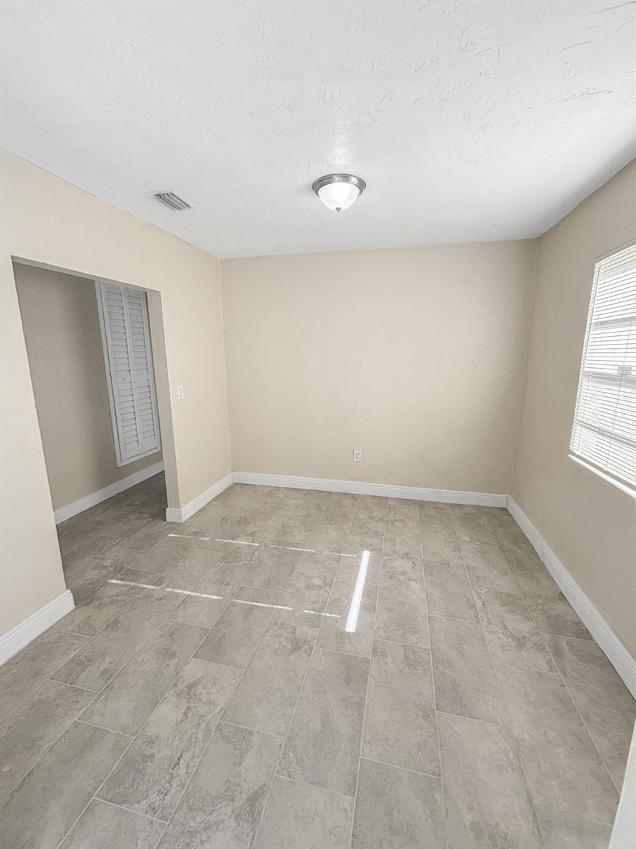 An empty room with beige walls, a flush-mount light fixture, and gray tile flooring — 3045 NW 68th Street NW, Miami FL 33147, MIAMI, FL
