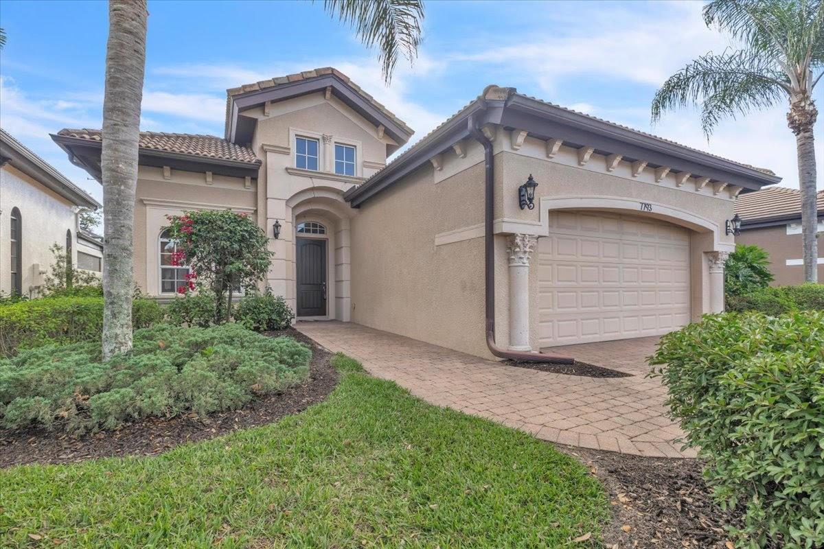 A single-story suburban house with a beige stucco exterior, arched entryway, and two-car garage — 7793 Ashton Road, Naples FL 34113, NAPLES, FL