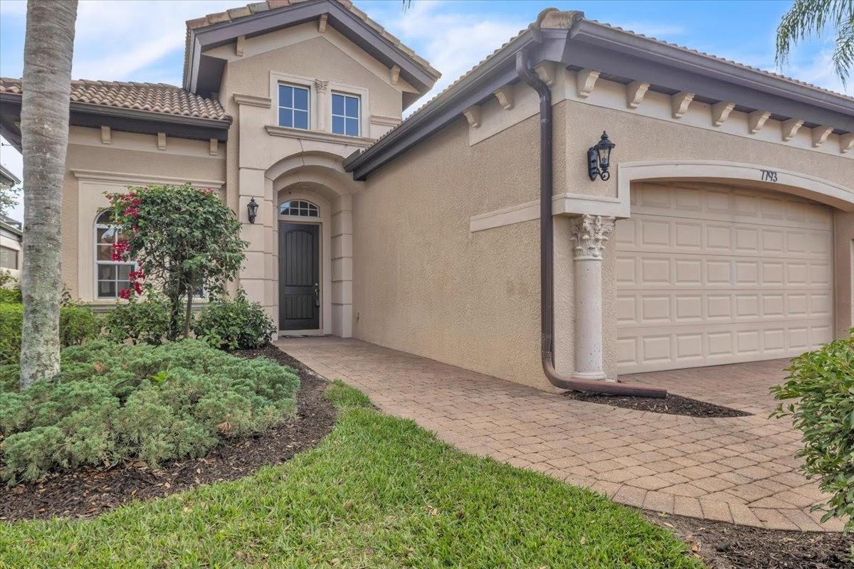 A beige stucco house with a tiled roof, arched entryway, and a paved driveway — 7793 Ashton Road, Naples FL 34113, NAPLES, FL